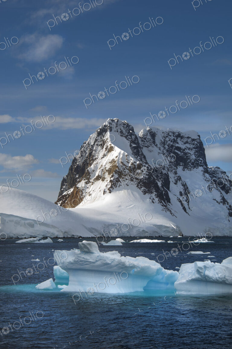Icebergs floating in the water off the rocky shore of Antactica.