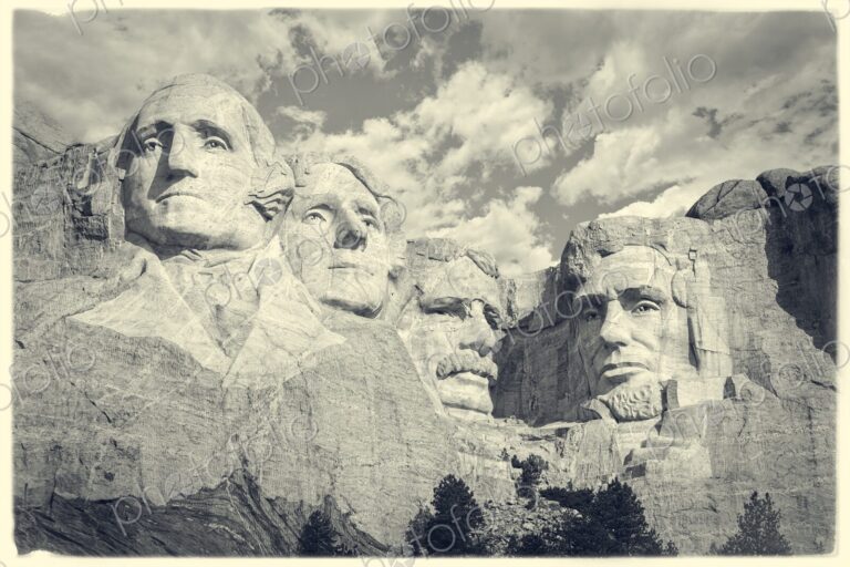 Iconic granite carvings of presidents on Mount Rushmore with clouds overhead and pines…