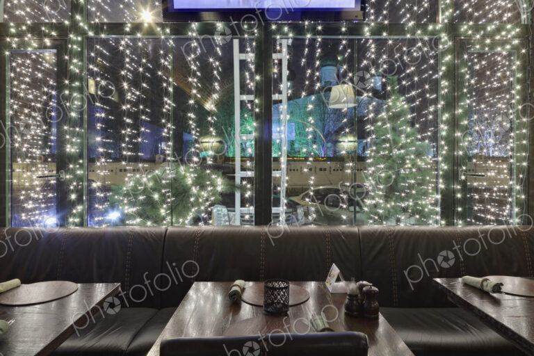Illuminated restaurant window at night, with tables and chairs.