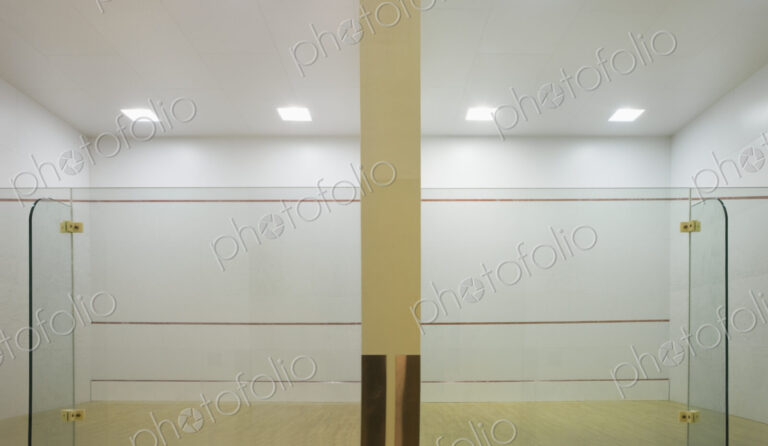 Indoor squash court with glass walls and markings.