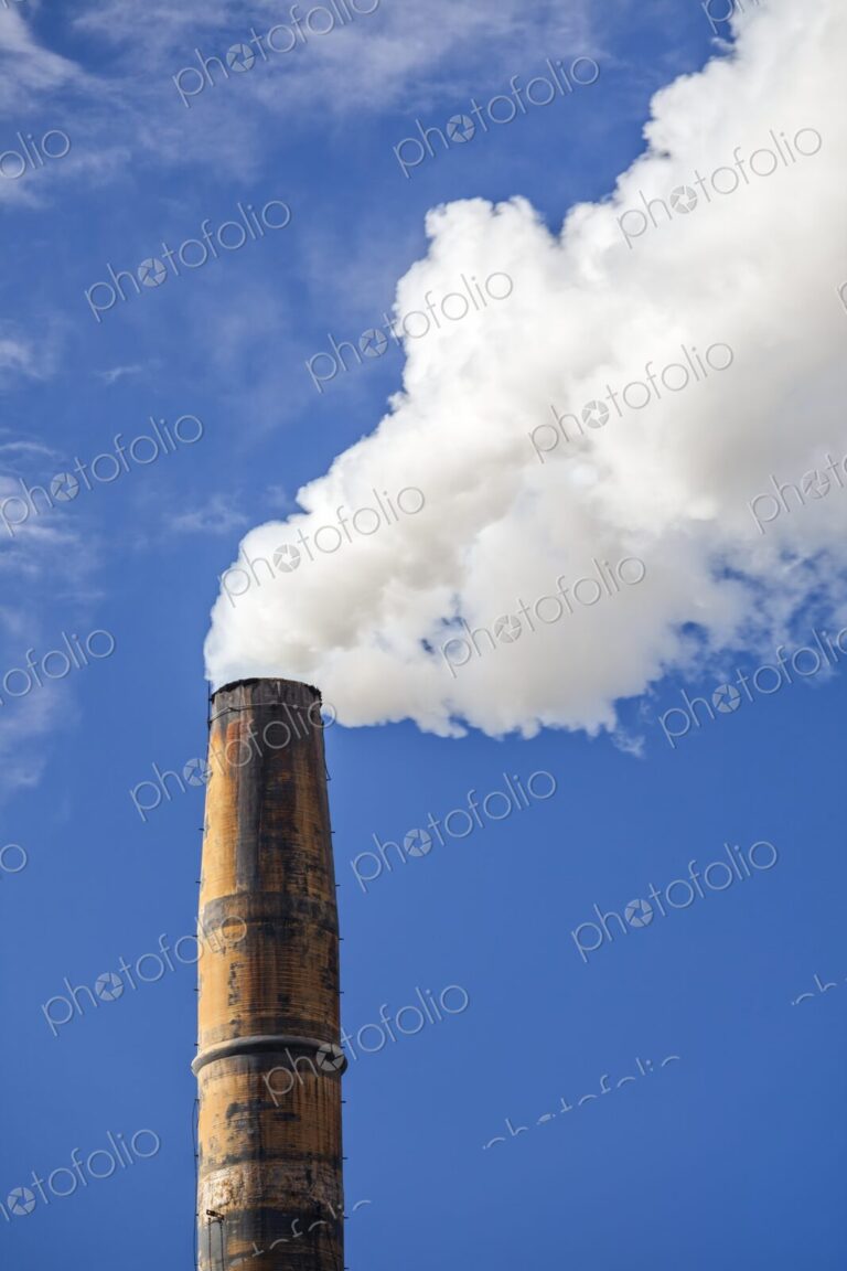 Industrial smokestack releasing white smoke against a clear blue sky in Port Angeles,…