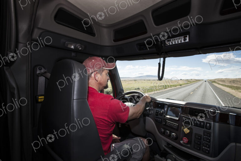 Interior cab view of a Caucasian man driving his commercial truck.