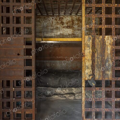 Interior of an antique frontier jail with rusty iron bars, an open door, padlock, and… Interior of an antique frontier jail with rusty iron bars, an open door, padlock, and…