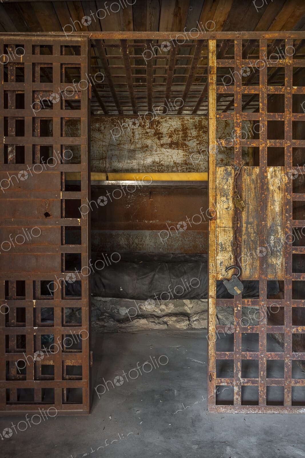 Interior of an antique frontier jail with rusty iron bars, an open door, padlock, and…