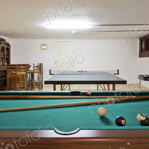 Interior view of a basement room with pool billiard and ping pong tables.