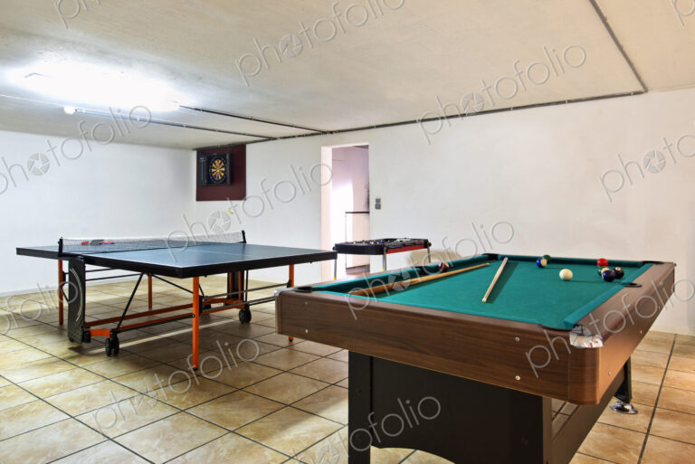 Interior view of a basement room with pool billiard and ping pong tables.