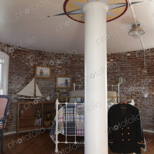 Interior view of a bedroom with exposed brick walls and metal bed in a lighthouse,…