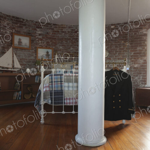 Interior view of a bedroom with exposed brick walls and metal bed in a lighthouse,…