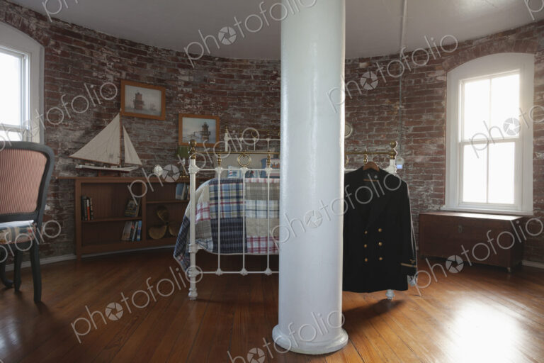 Interior view of a bedroom with exposed brick walls and metal bed in a lighthouse,…
