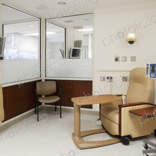 Interior view of a hospital treatment cubicle with a chair and a drip treatment stand,…