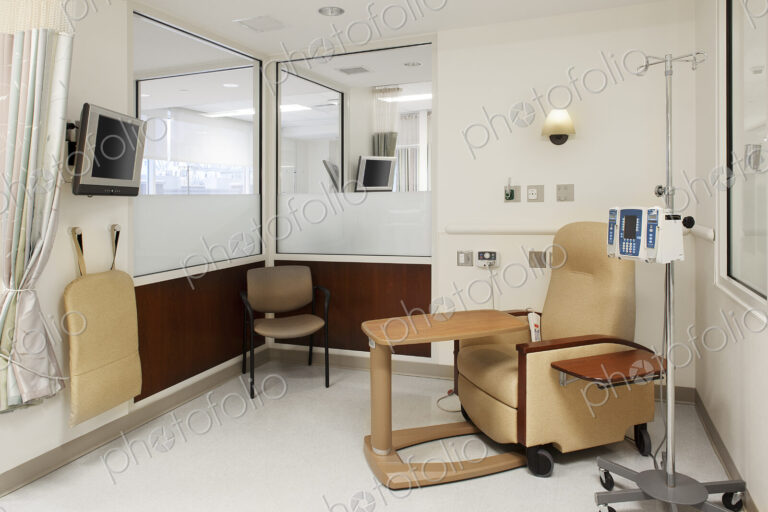 Interior view of a hospital treatment cubicle with a chair and a drip treatment stand,…