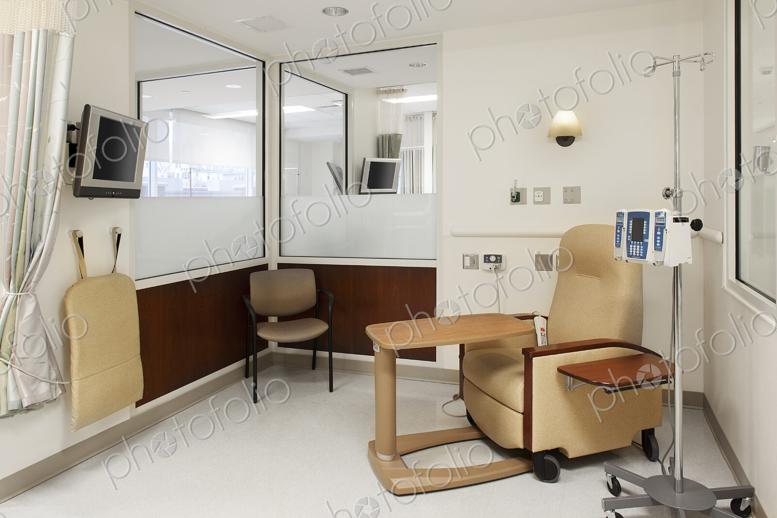 Interior view of a hospital treatment cubicle with a chair and a drip treatment stand,…