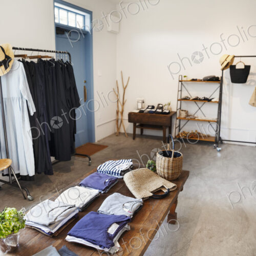 Interior view of a small fashion boutique, with T-Shirts on a coffee table and dresses…