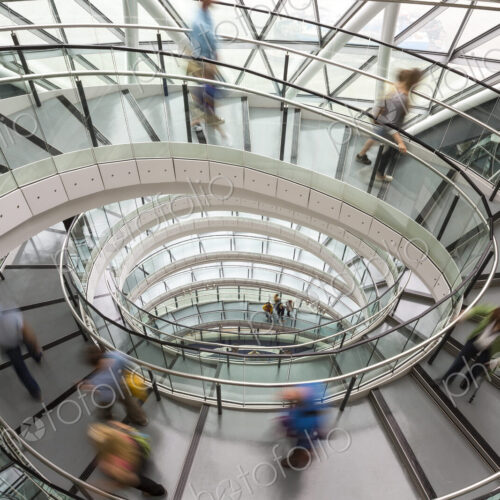 Interior view of building with people walking along glass and metal spiral staircase. Interior view of building with people walking along glass and metal spiral staircase.