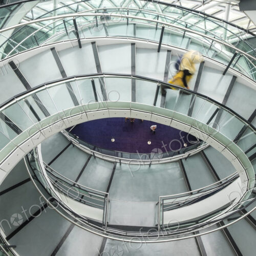 Interior view of building with person walking along glass and metal spiral staircase. Interior view of building with person walking along glass and metal spiral staircase.
