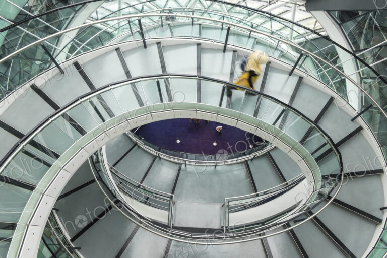 Interior view of building with person walking along glass and metal spiral staircase.