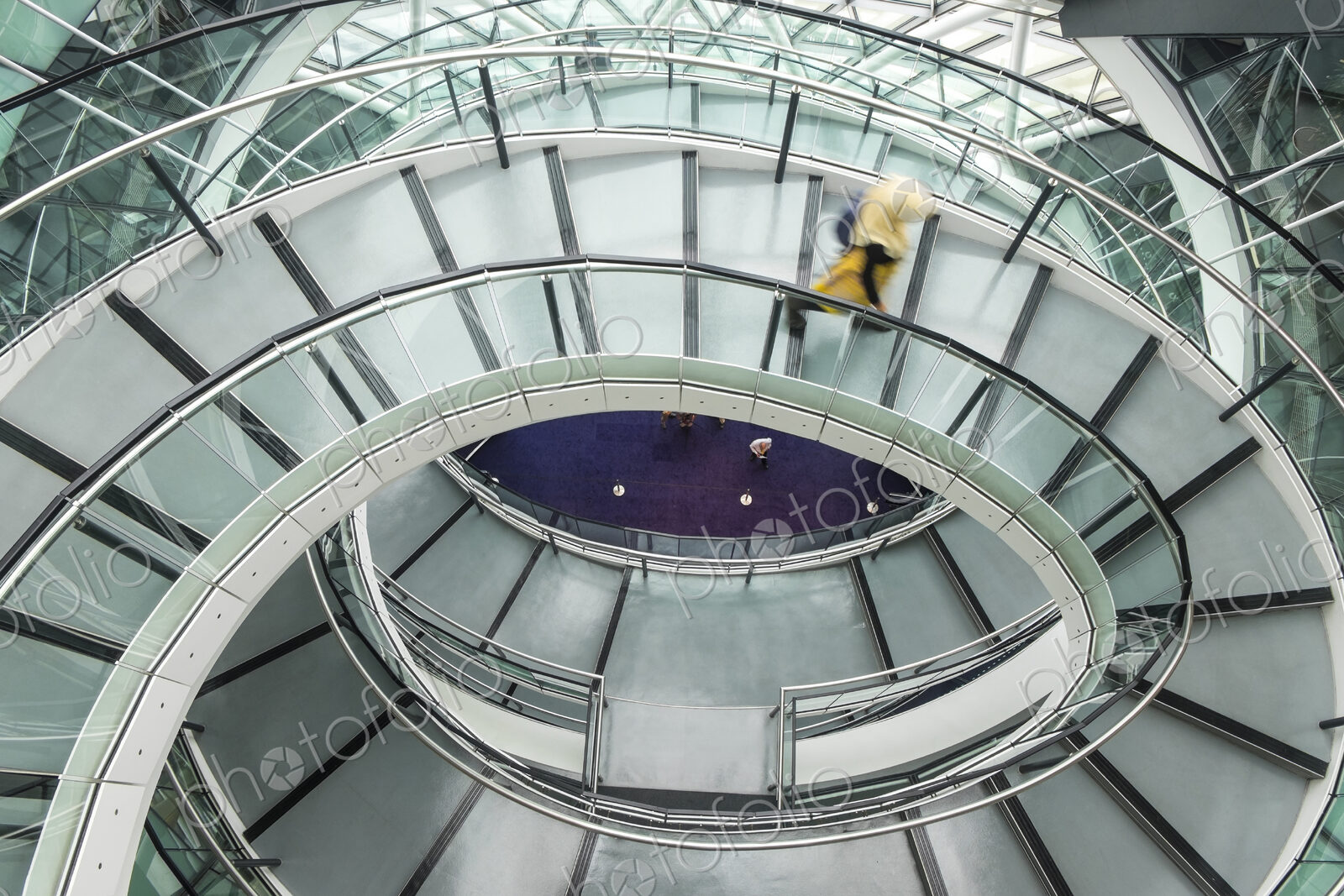 Interior view of building with person walking along glass and metal spiral staircase.