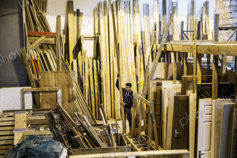 Interior view of warehouse with stacks of wooden planks, young man working.