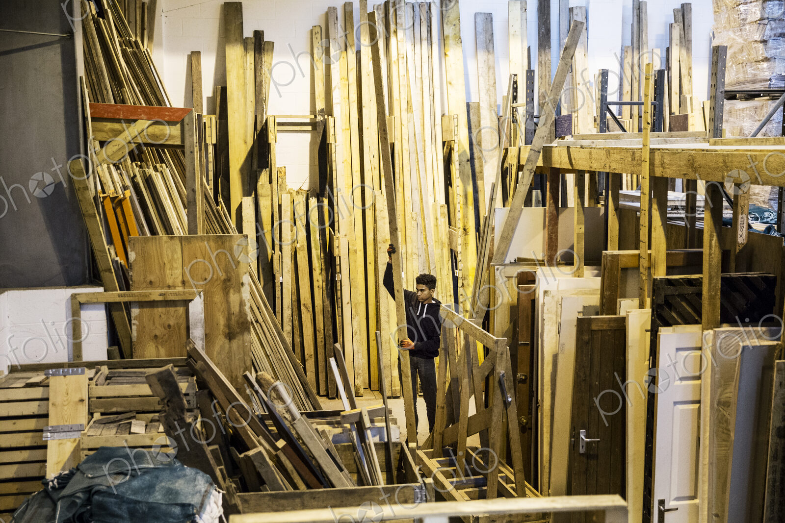 Interior view of warehouse with stacks of wooden planks, young man working.