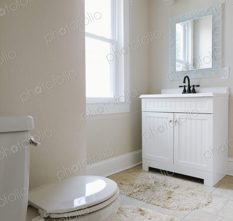 Interior view of white bathroom with toilet and vanity sink unit with taps.