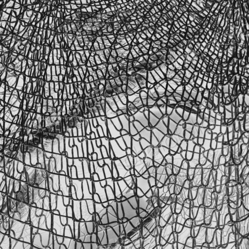 Inverted black and white image of commercial fishnets and ropes on a fishing quay.