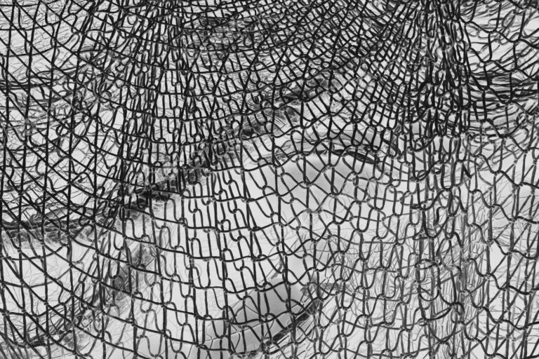Inverted black and white image of commercial fishnets and ropes on a fishing quay.