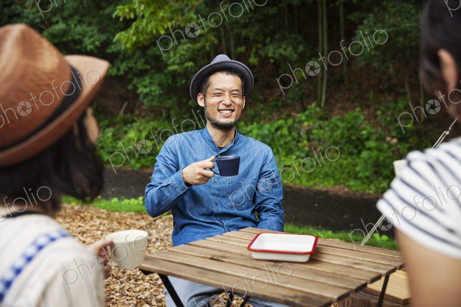 Japanese man and two women sitting outdoors at a table, drinking coffee.