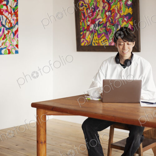 Japanese man siting at a table in an art gallery, looking at laptop computer.