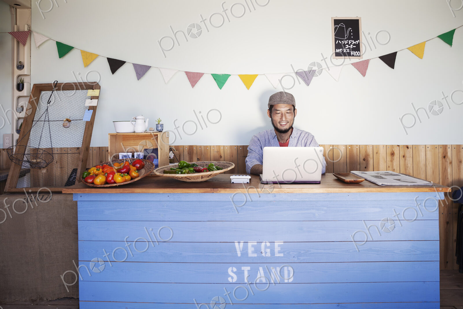 Japanese man sitting behind counter of a farm shop, working on laptop computer.