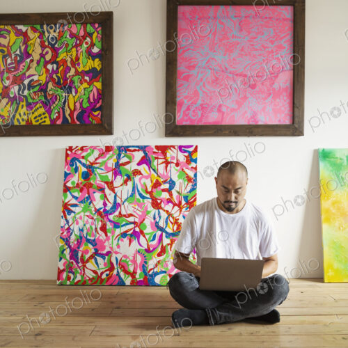 Japanese man sitting on floor of art gallery, working on laptop computer.
