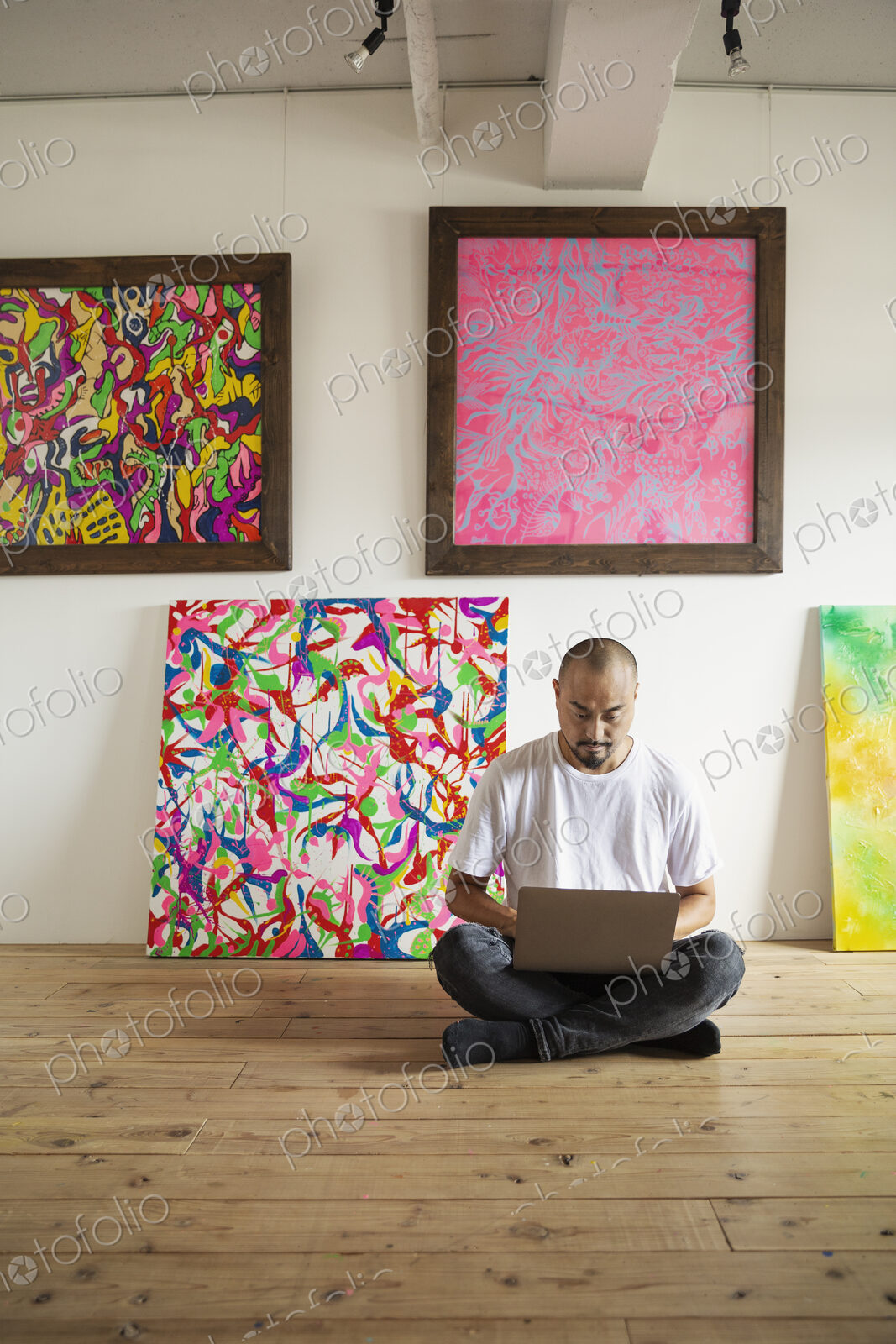 Japanese man sitting on floor of art gallery, working on laptop computer.