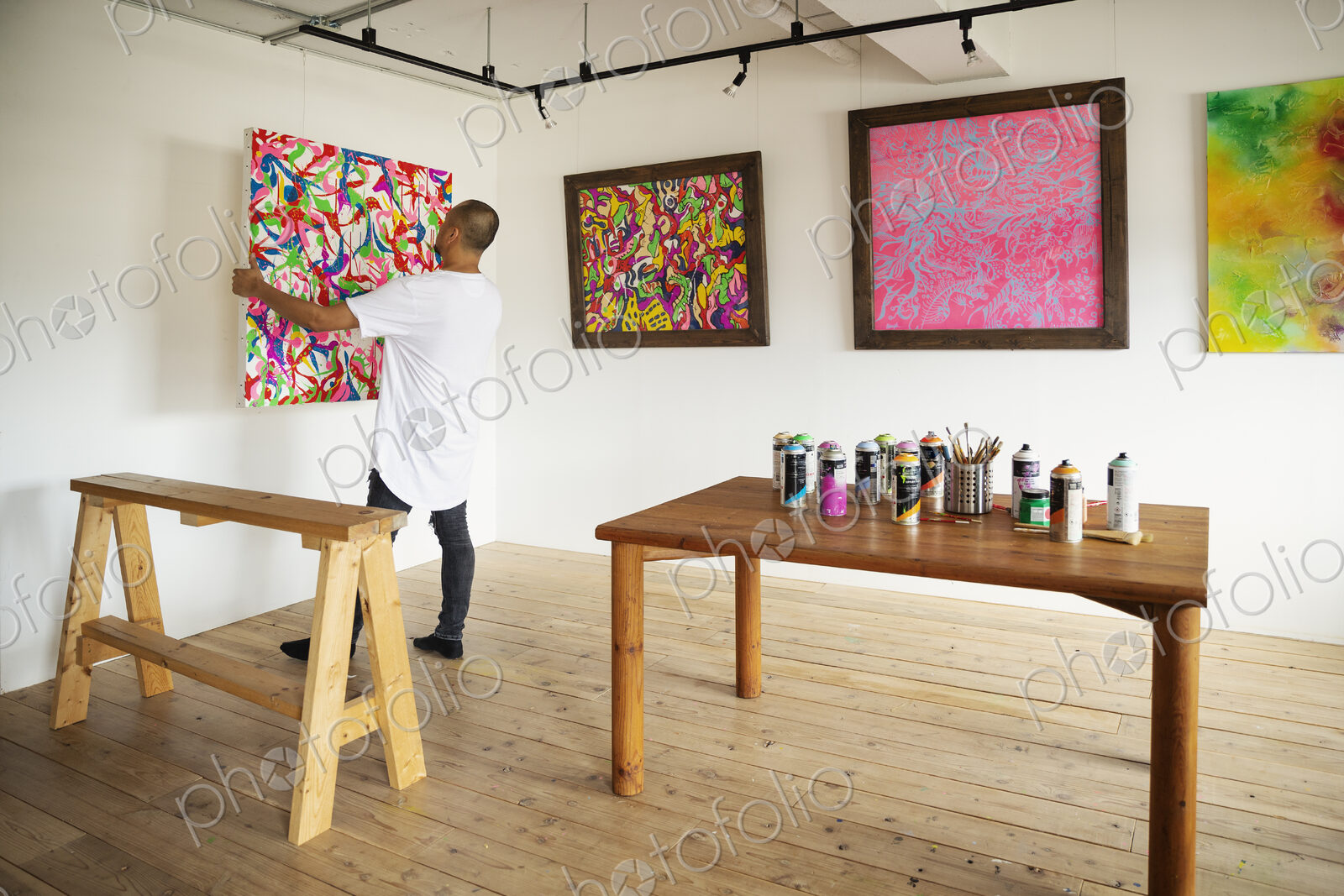 Japanese man standing in art gallery, hanging colourful painting on white wall.