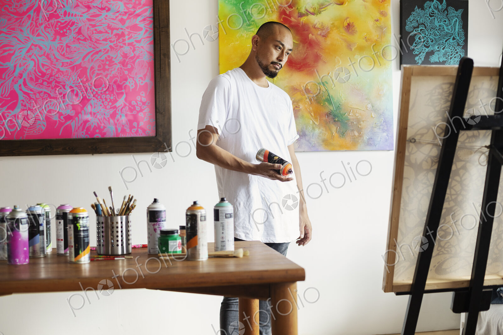 Japanese man standing in art gallery, holding can of spray paint, looking at artwork…