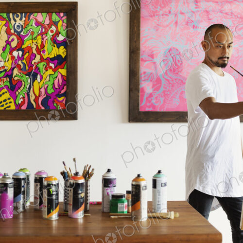 Japanese man standing in art gallery, holding paintbrush, working on artwork on easel.