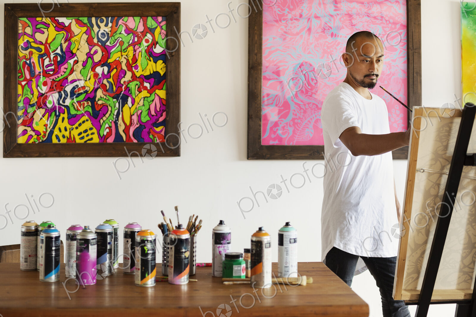 Japanese man standing in art gallery, holding paintbrush, working on artwork on easel.