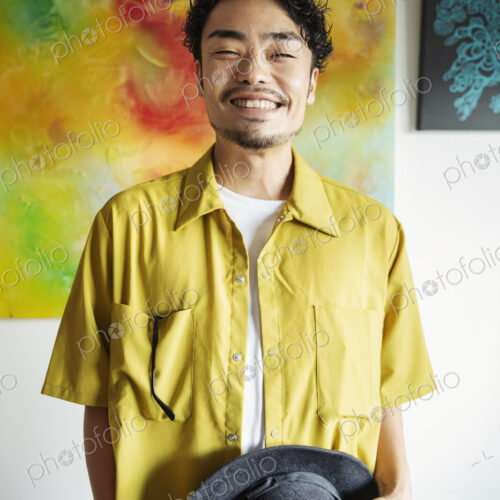 Japanese man standing in front of abstract painting in an art gallery, smiling at camera.