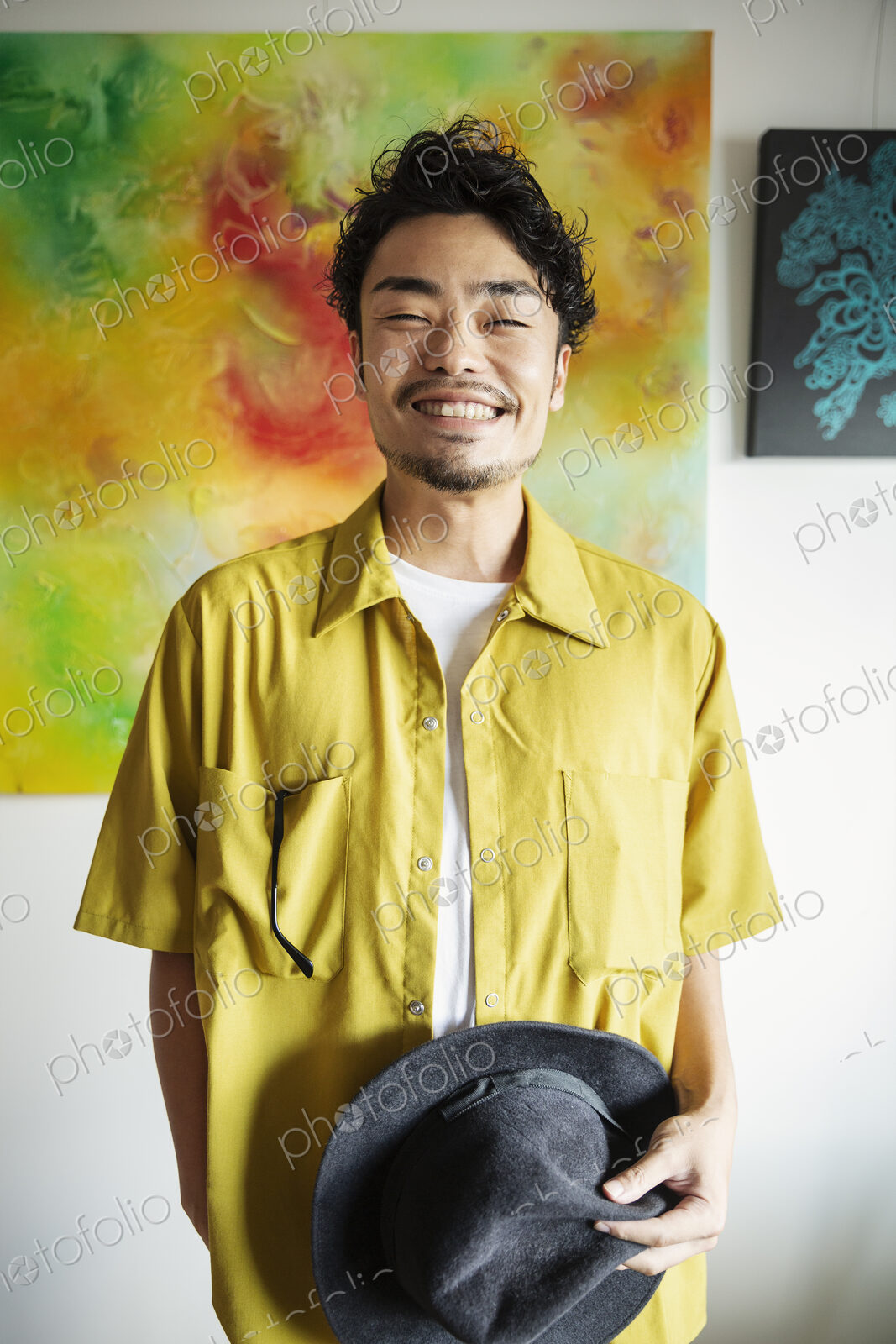 Japanese man standing in front of abstract painting in an art gallery, smiling at camera.