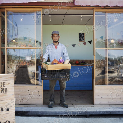 Japanese man standing outside a farm shop, holding crate with fresh vegetables,… Japanese man standing outside a farm shop, holding crate with fresh vegetables,…