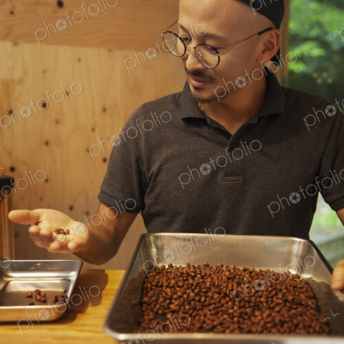 Japanese man wearing baseball cap and glasses standing in an Eco Cafe, checking… Japanese man wearing baseball cap and glasses standing in an Eco Cafe, checking…
