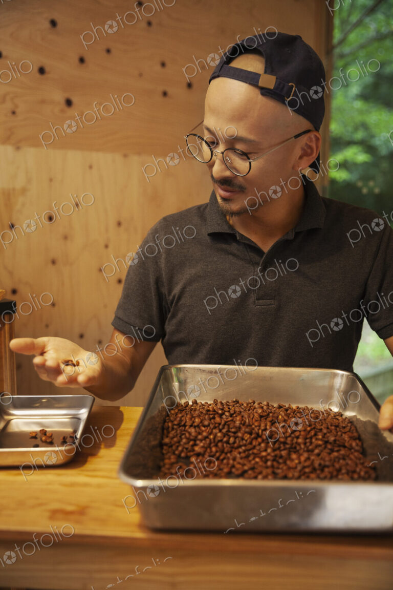 Japanese man wearing baseball cap and glasses standing in an Eco Cafe, checking…