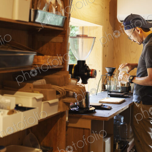 Japanese man wearing baseball cap and glasses standing in an Eco Cafe, preparing cup… Japanese man wearing baseball cap and glasses standing in an Eco Cafe, preparing cup…