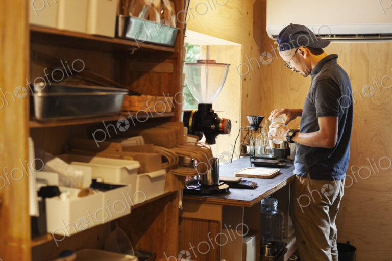 Japanese man wearing baseball cap and glasses standing in an Eco Cafe, preparing cup…