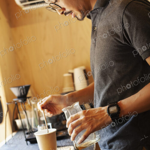 Japanese man wearing baseball cap and glasses standing in an Eco Cafe, preparing cup…