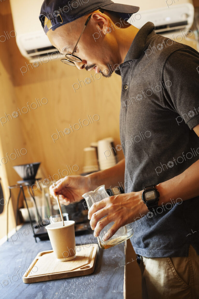 Japanese man wearing baseball cap and glasses standing in an Eco Cafe, preparing cup…
