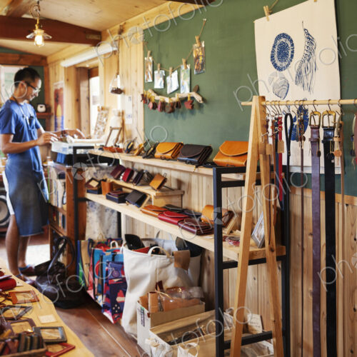 Japanese man wearing blue apron and glasses standing in a leather shop.