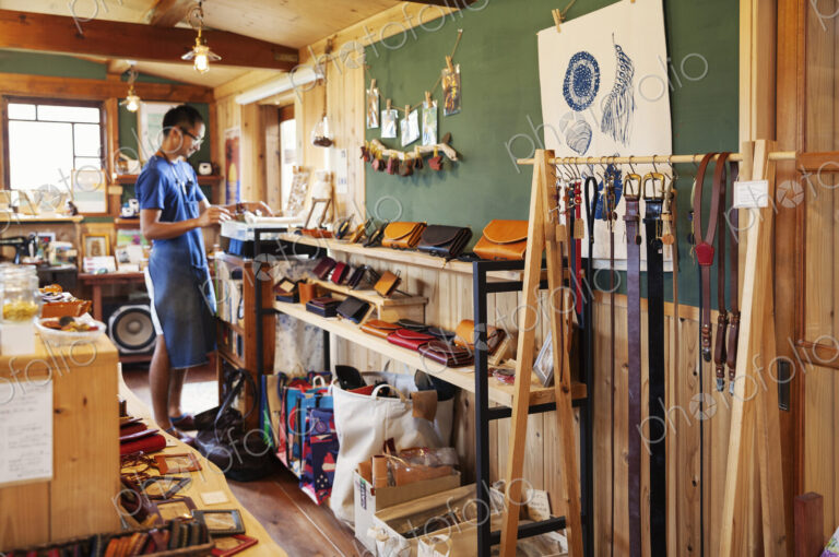 Japanese man wearing blue apron and glasses standing in a leather shop.