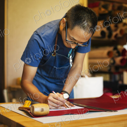 Japanese man wearing blue apron working in a leather shop. Japanese man wearing blue apron working in a leather shop.