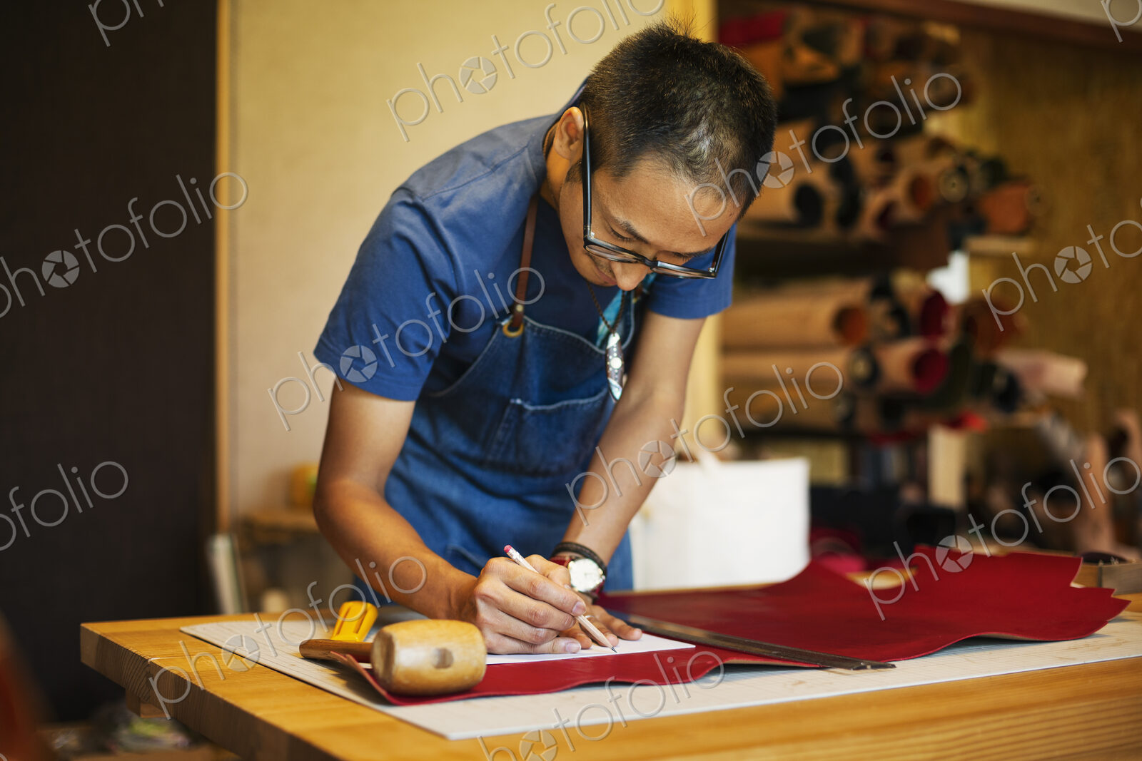 Japanese man wearing blue apron working in a leather shop.