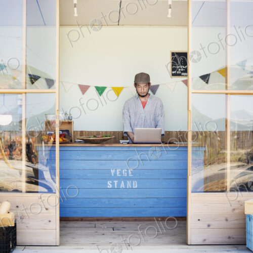 Japanese man wearing cap standing behind counter in farm shop. Japanese man wearing cap standing behind counter in farm shop.