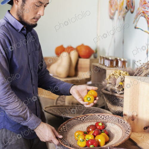 Japanese man wearing cap standing in farm shop, holding bowl with fresh vegetables. Japanese man wearing cap standing in farm shop, holding bowl with fresh vegetables.
